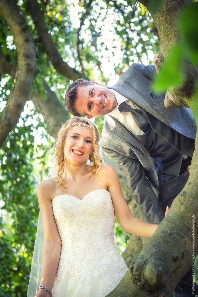 Hochzeitsfotografie - Brautpaar mit blonder Braut auf altem Baum im Grünen